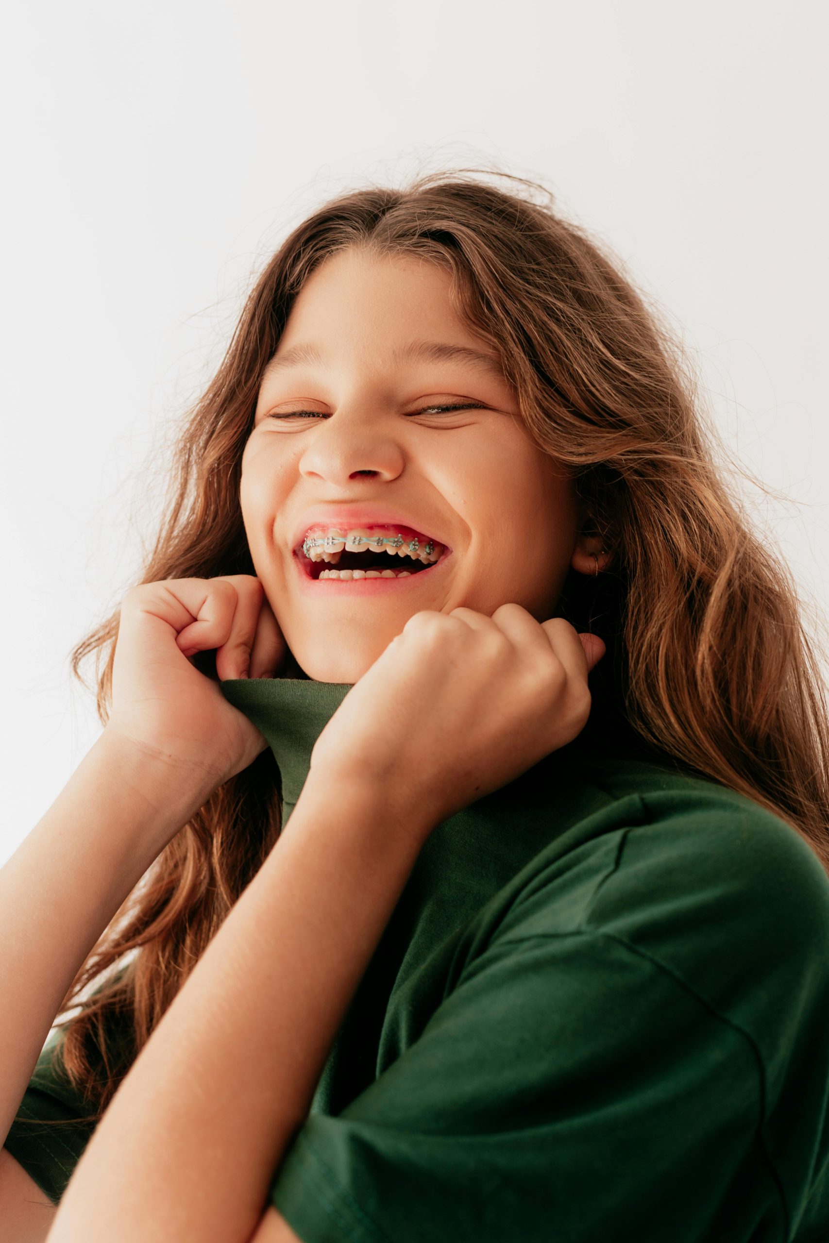 Smiling teenage girl with braces, wearing a green shirt, showing healthy teeth